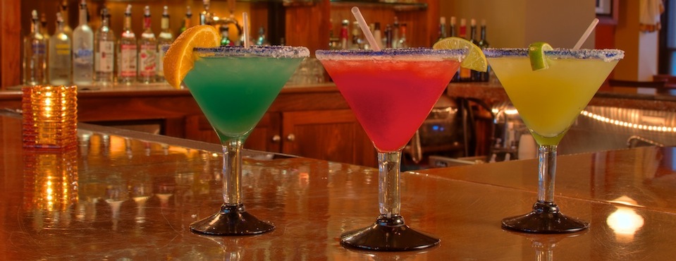Three colorful margaritas sitting on a bar.